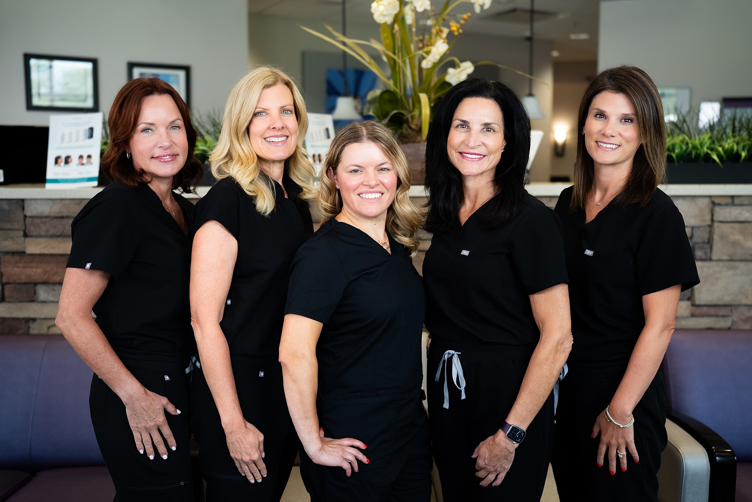 Five women in black scrubs smiling together.